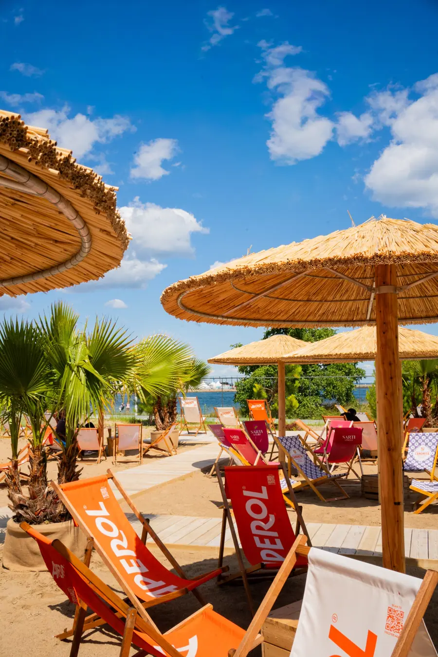 Strohschirme, Palmen und bunte Liegestühle am VIEW Beach mit Blick aufs Wasser
